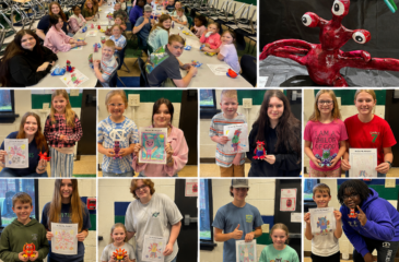 First grade students and high school art students pose with colorful monster drawings and matching handmade monster sculptures.